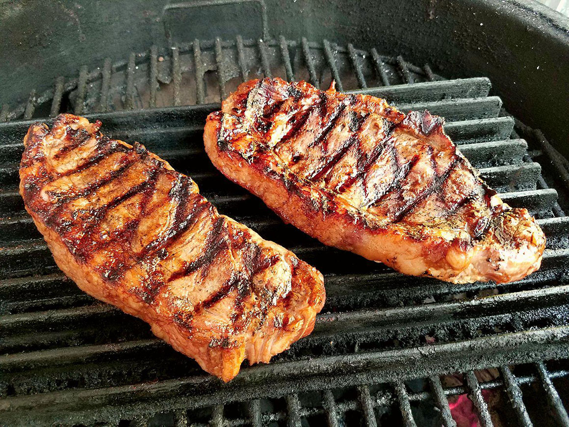 two steaks cooking on a grill