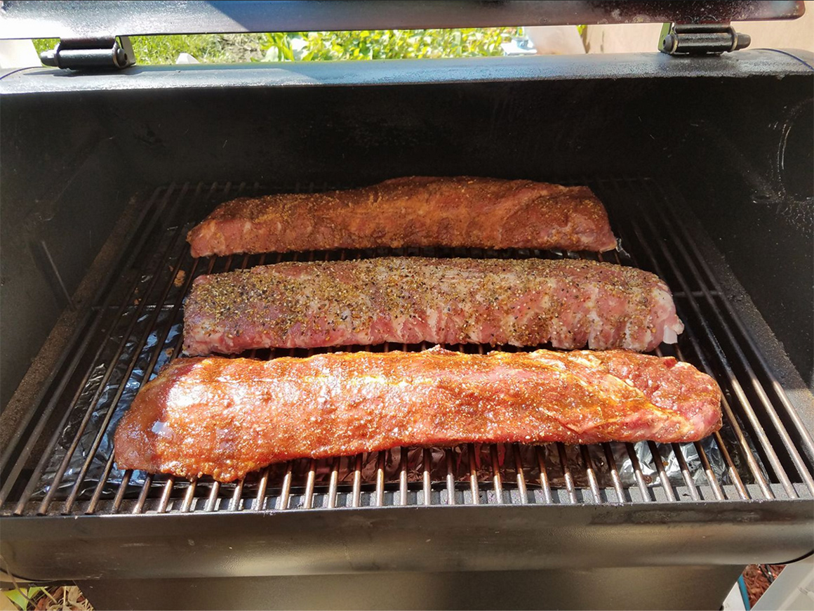 three racks of seasoned ribs cooking on a grill