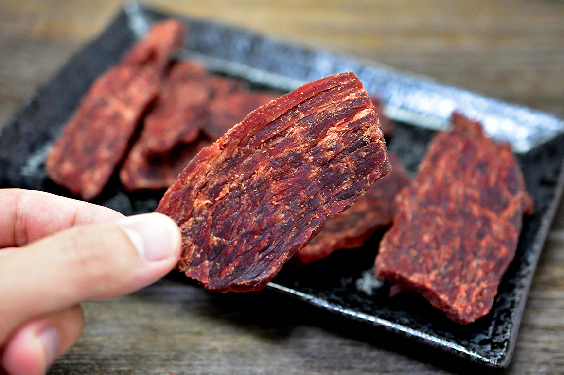 a person picking up a piece of Dried Peppered Beef Jerky