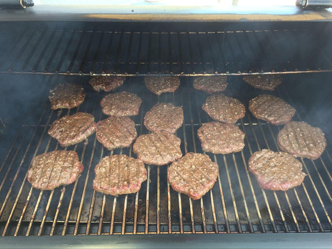 a grill full of cooking burgers