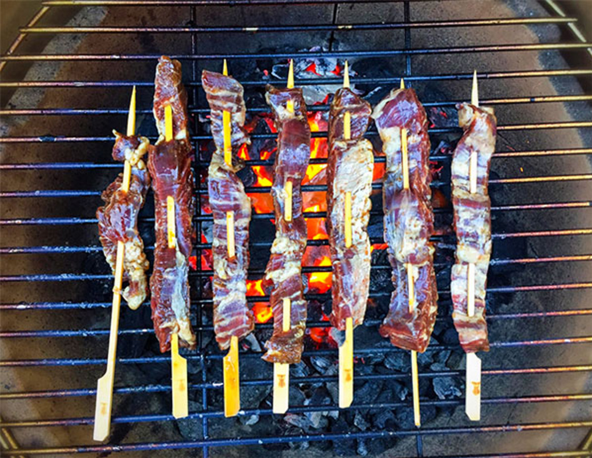 a line of several kebabs cooking on a grill