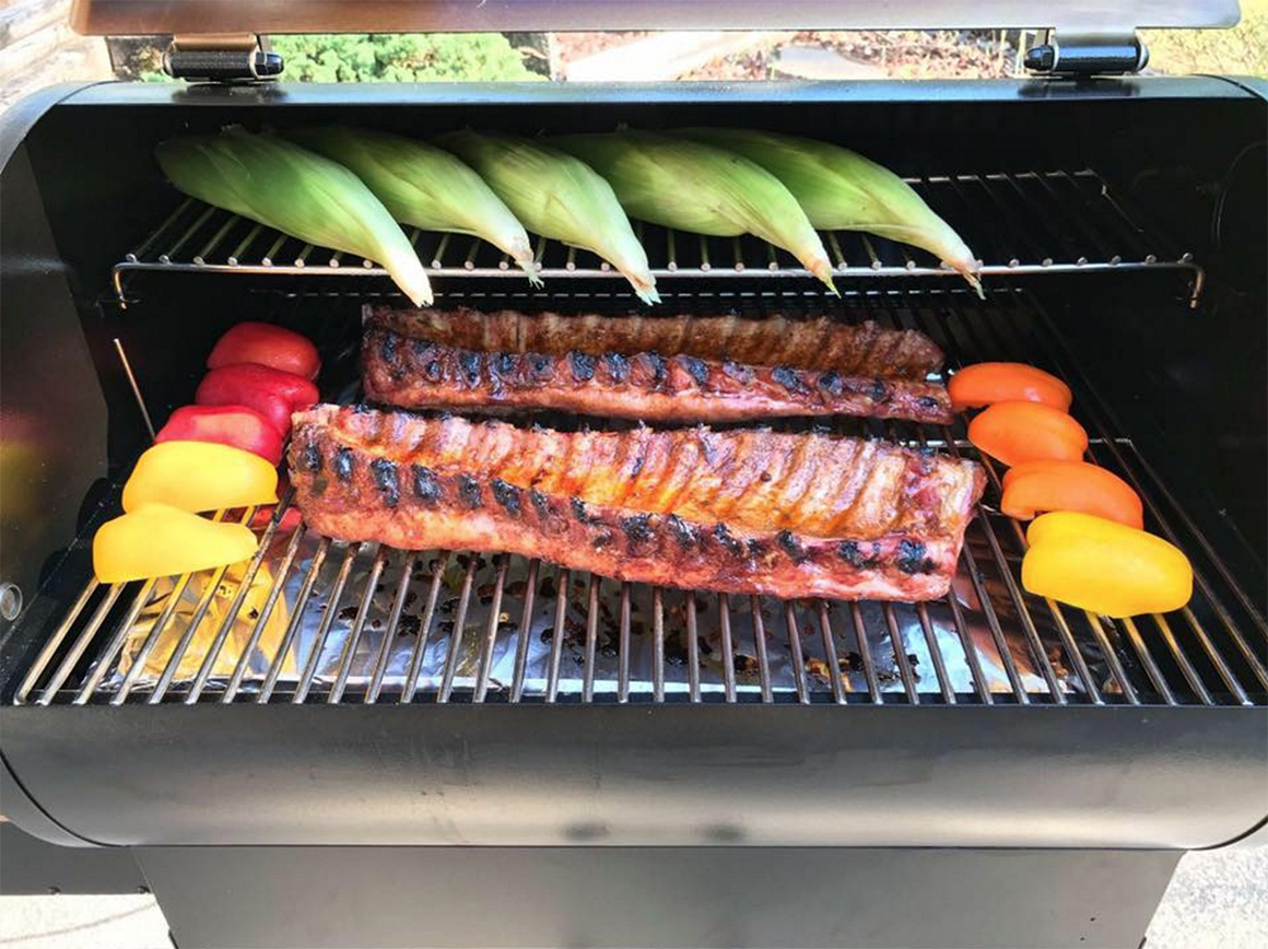 a rack of ribs on a grill with corn and bell peppers